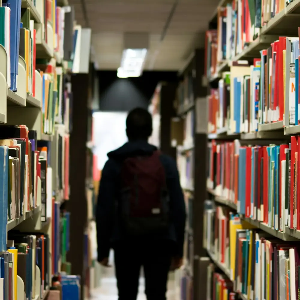 Student walking between tall library shelves